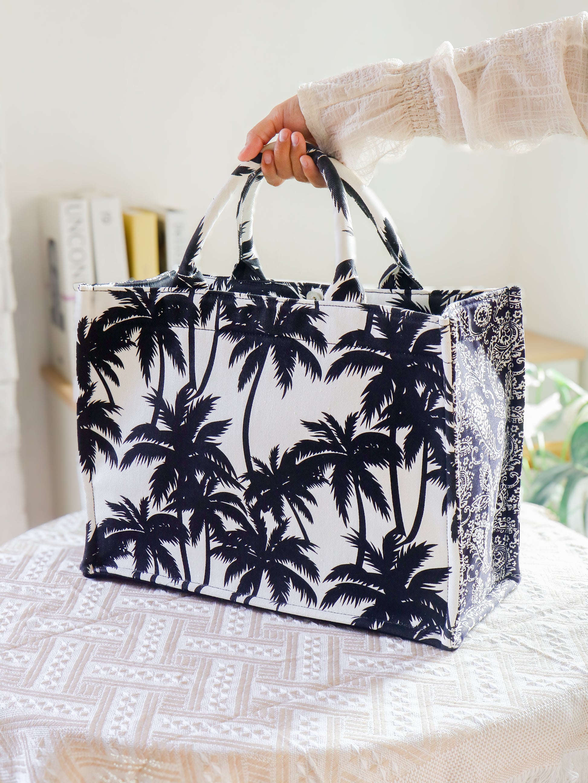 Tote bag with palm tree design held by a person on a white surface.