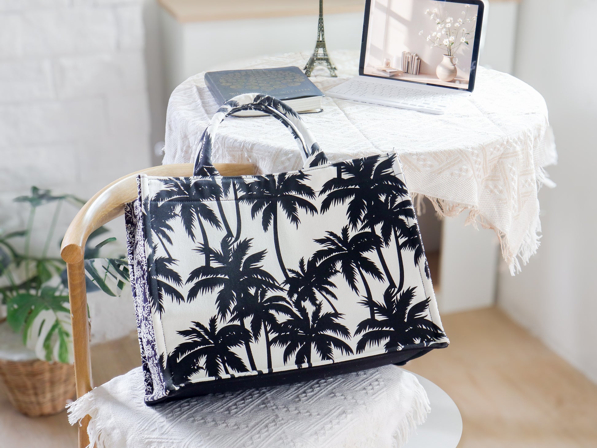 Tote bag with black palm tree design on a chair in a room with a desk and Eiffel Tower model.