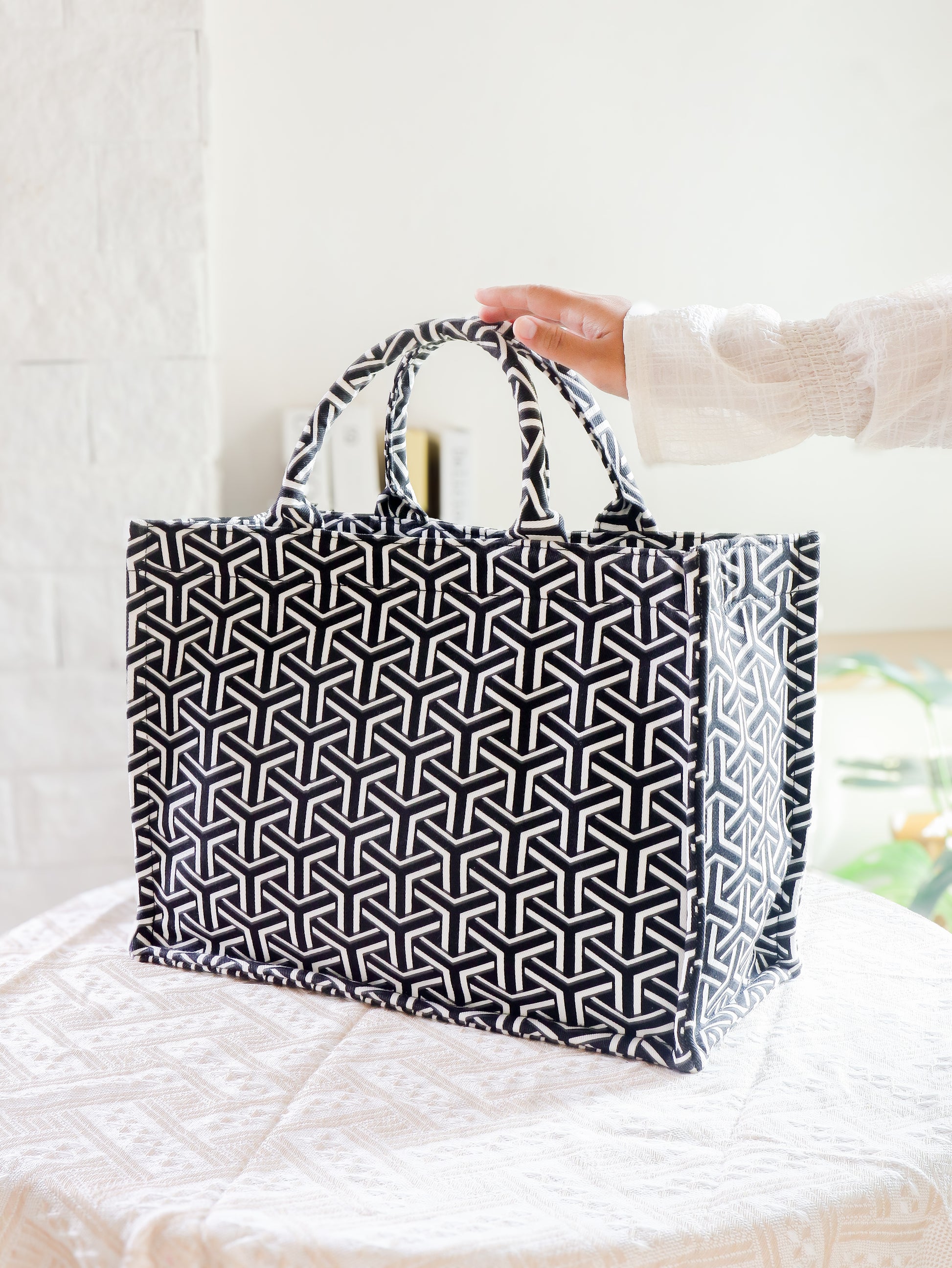 Black and white geometric patterned tote bag held by a person on a light background