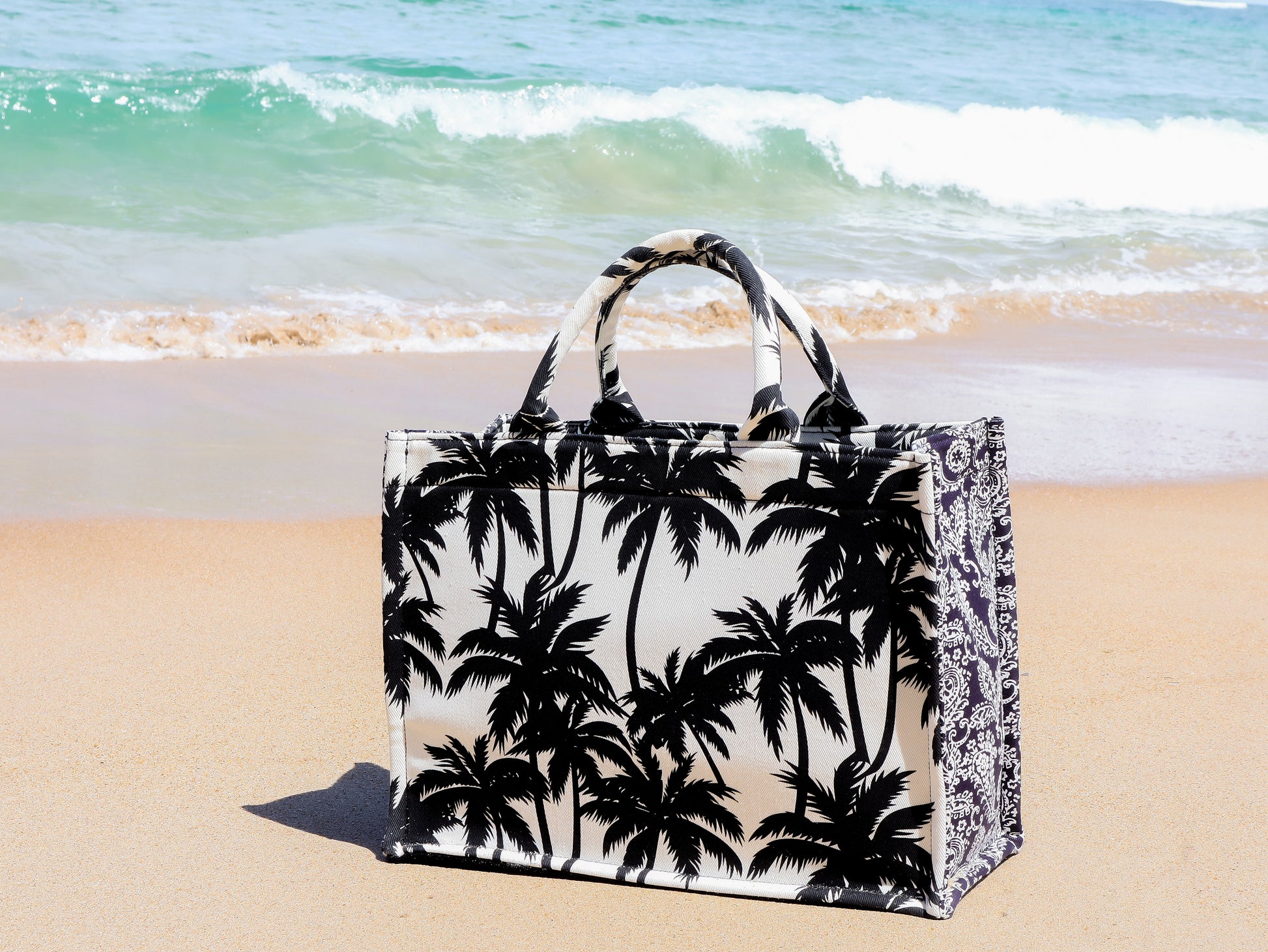 Tote bag with palm tree design on a sandy beach with ocean waves in the background