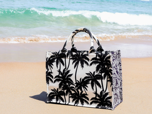 Tote bag with palm tree design on a sandy beach with ocean waves in the background
