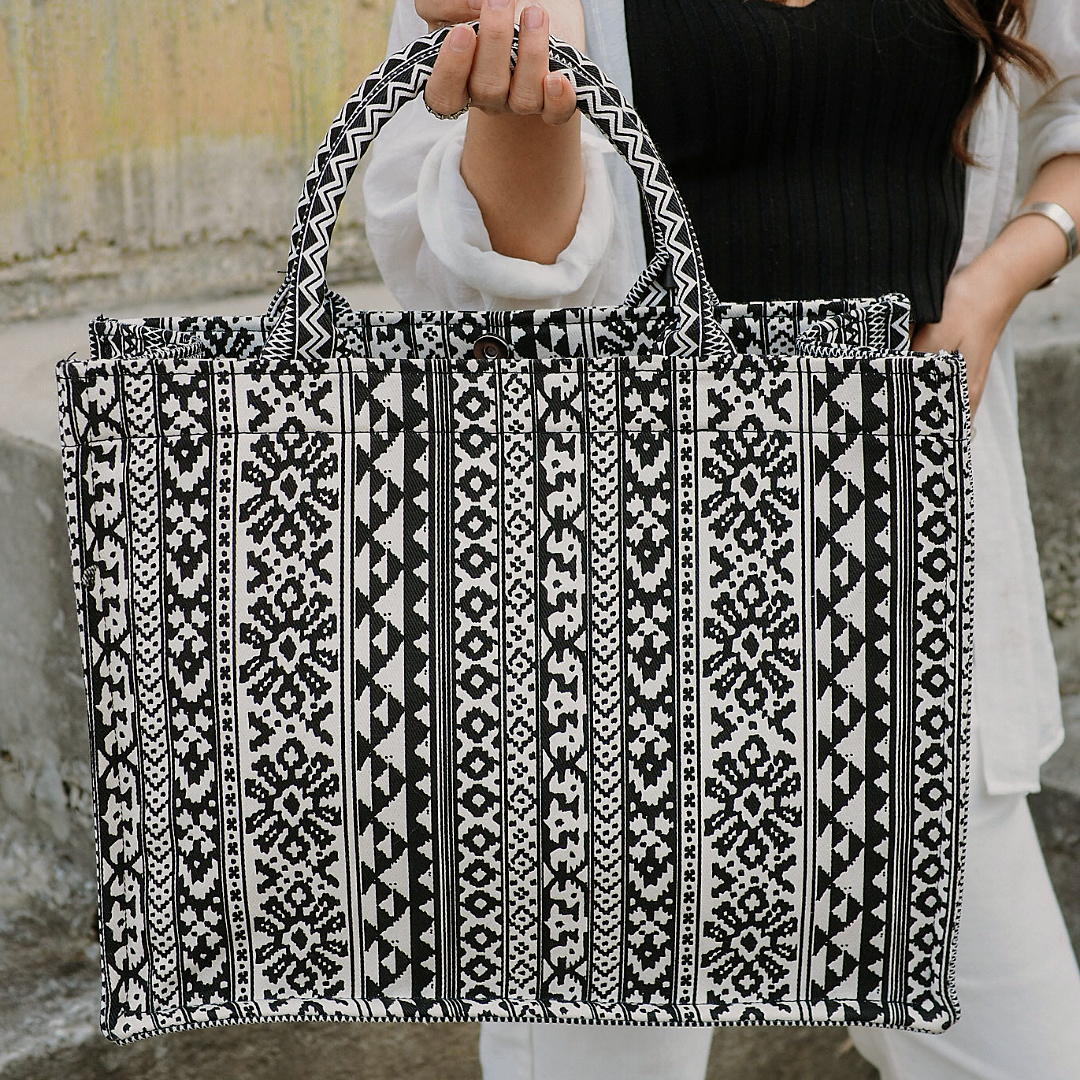 A person holding a large black and white geometric patterned canvas tote bag.