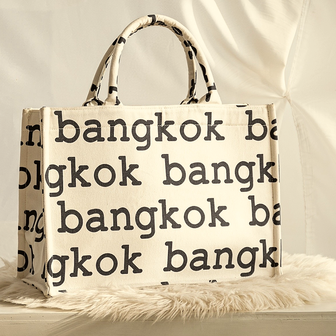 A woman in a red dress holding a large canvas tote bag with 'bangkok' printed in blue letters.