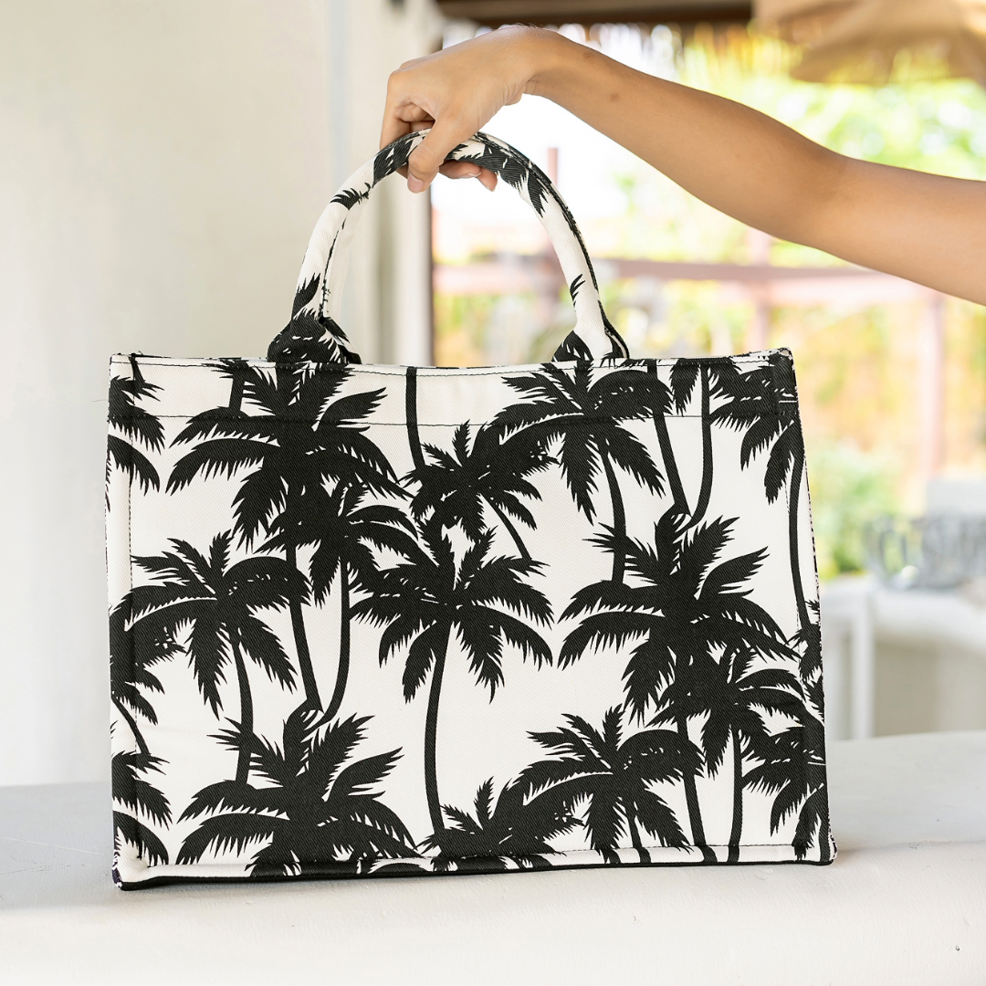 A woman holding a black and white canvas tote bag with a bold black palm tree print.