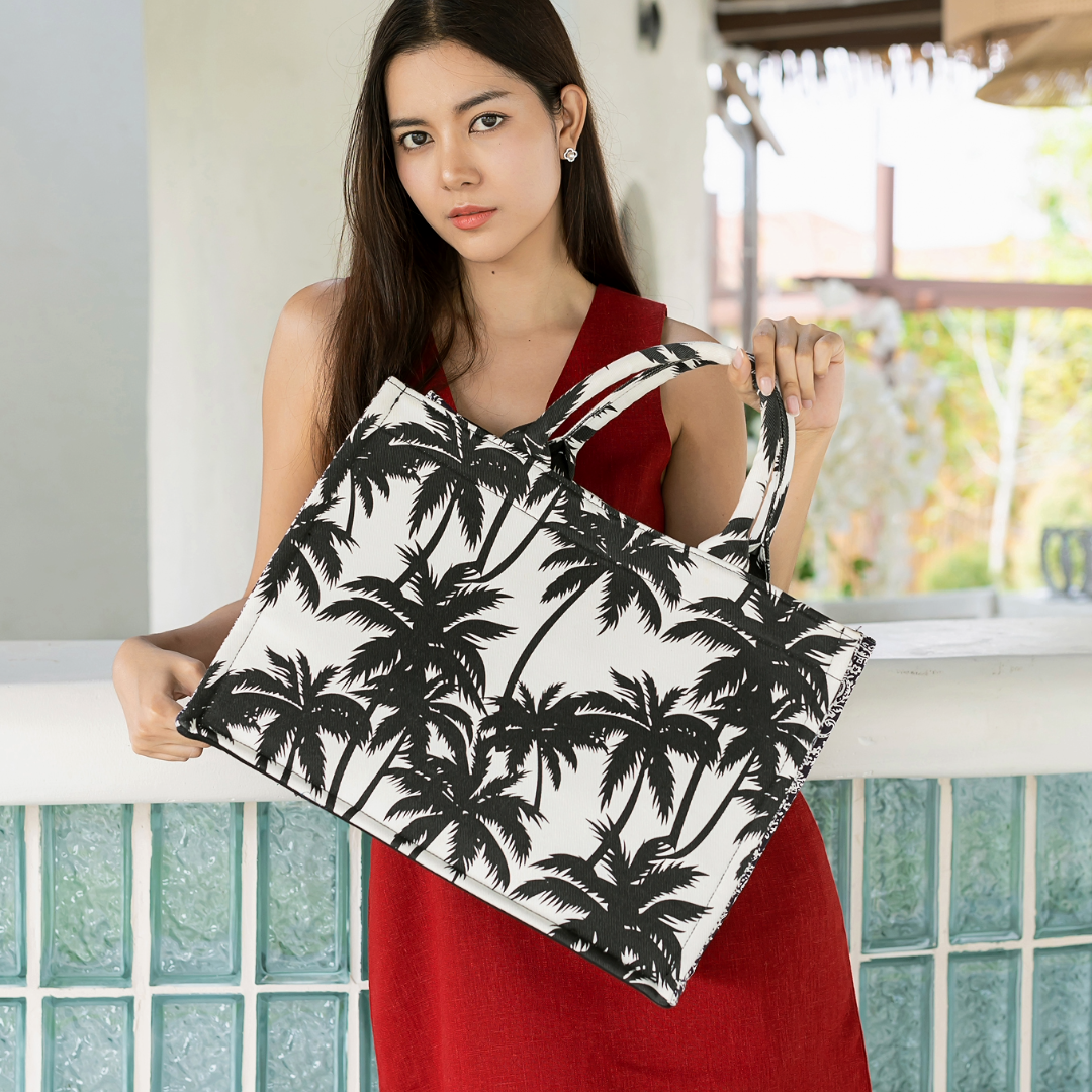 A woman holding a black and white canvas tote bag with a bold black palm tree print.