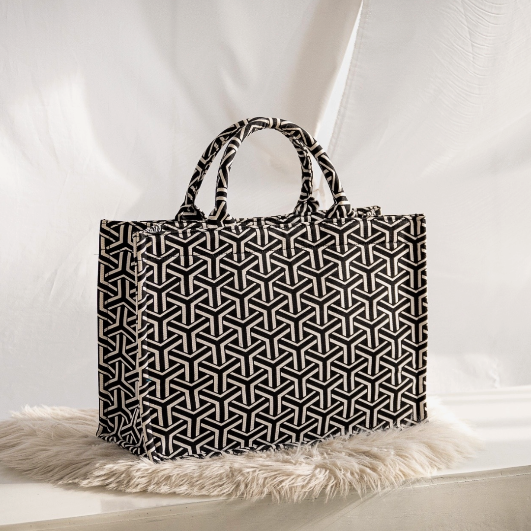 A black and white geometric patterned tote bag placed on a white furry surface.