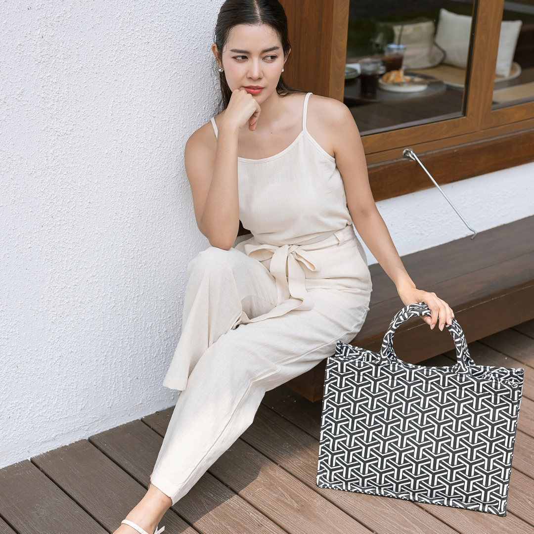 Woman in a white outfit holding a black and white patterned bag on a wooden floor.
