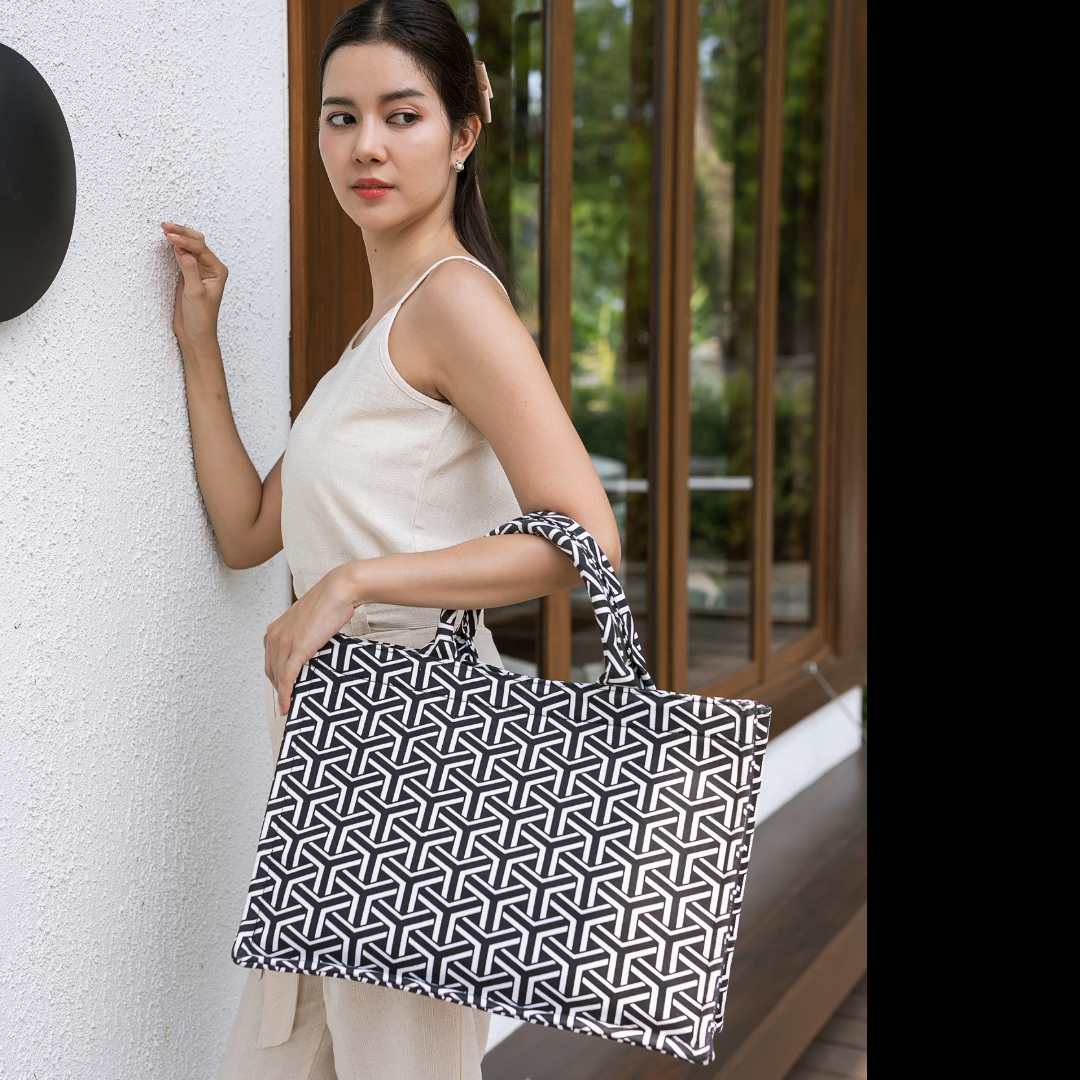 Woman holding a black and white geometric patterned bag against a white wall.