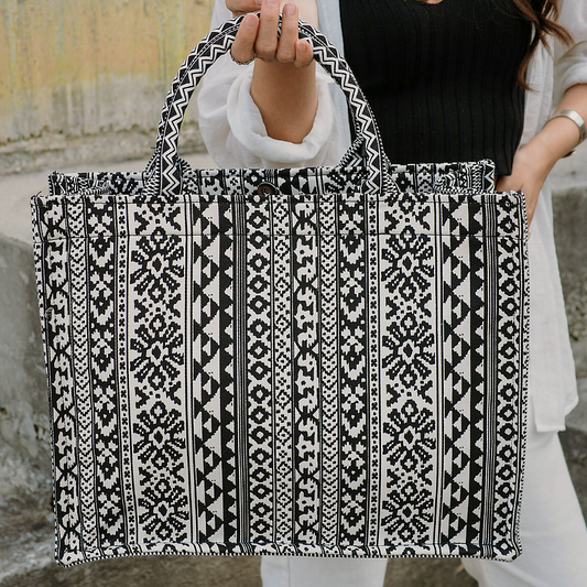 A person holding a large black and white geometric patterned canvas tote bag.