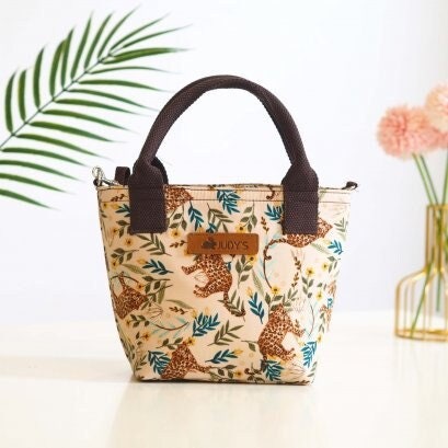 Small Top Handle handbag with shoulder strap in a jungle print with leopards and leaves on a light background.